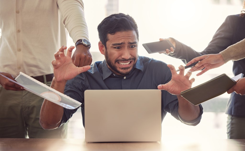 A man looks stressed at his computer as many people demand his attention.